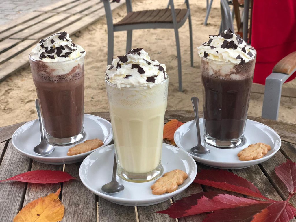 Drei heiße Schokoladen mit Sahne und Herbstlaub auf dem Tisch