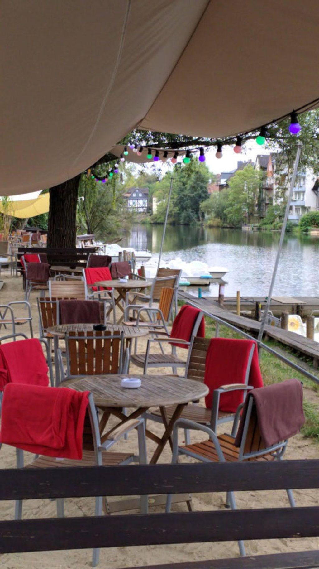 Gemütliche Sitzplätze mit roten Decken und bunten Lichterketten am Fluss