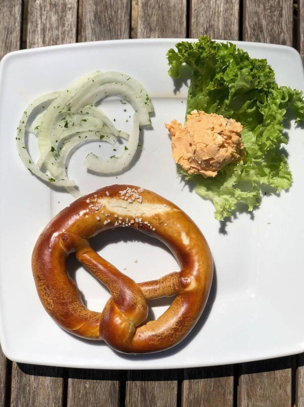 Frische Brezel mit Obatzda, Salat und Zwiebeln auf Holztisch