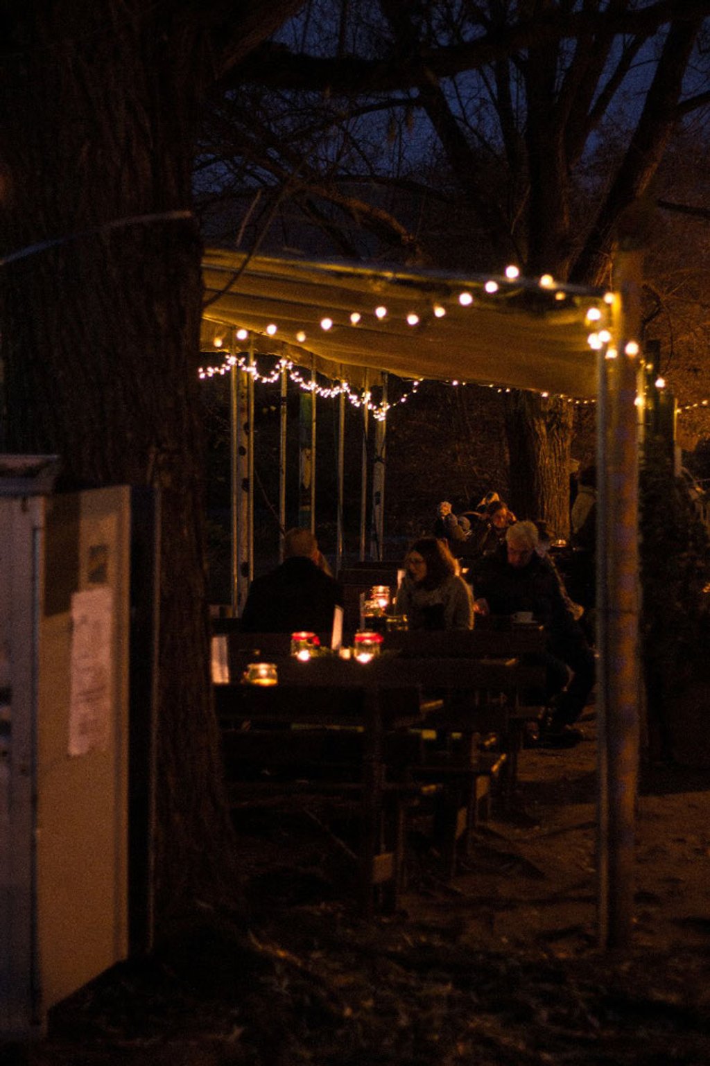 Gäste am Abend unter dem Sonnensegel mit Lichterketten und Kerzen